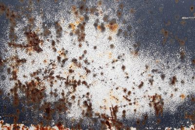 Orange rust dots bloom, white paint fades on dark metal, decay claims the steel