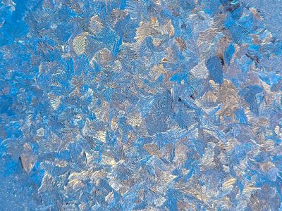 Pale frost holds the light, crystalline paths trace the pane, cold grit meets the eye