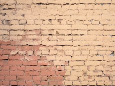 Pale paint coats the clay, rosy hues bleed through the cracks, time erodes the wall