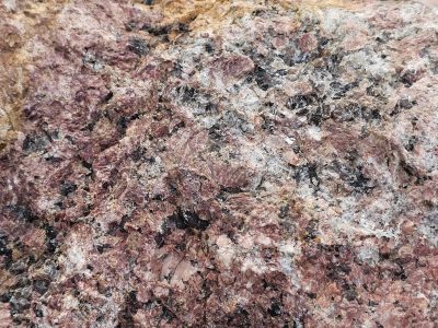 Pink crystals shimmer, dark specks ground the rugged face, ancient stone reveals