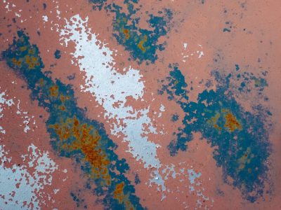 Pink paint peels away, blue and rust bloom on the steel, weathered metal fades