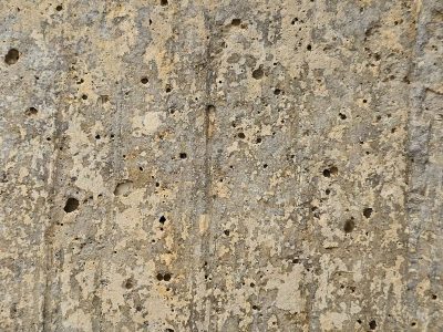 Pitted concrete wall, weathered surface wears away, shadows hide in holes