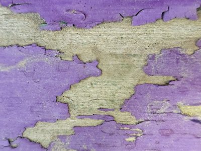 Purple paint flakes off, weathered grain beneath the skin, time peels back the layers