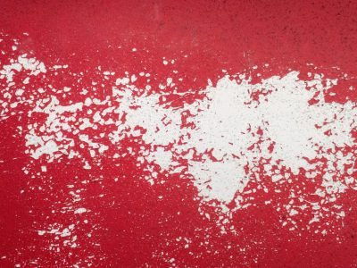 Red chips fall away, white shows through the scarlet skin, time strips back the paint