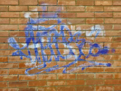 Red clay bricks aligned, blue spray drifts across the wall, urban marks remain