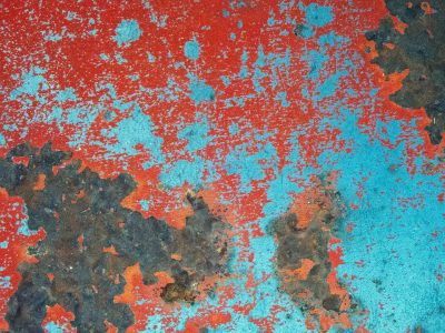 Bright red paint decays, turquoise sky on rusted ground, iron wears away