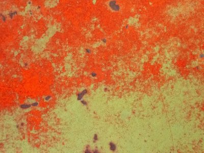 Red flakes wear away, pale green layers show beneath, dark pits mark the steel