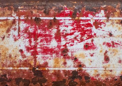 Red paint chips away, oxidation scars the steel, white lines drift in rust