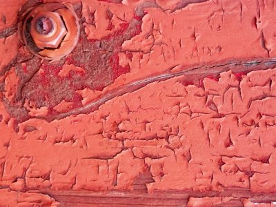 Red paint curls away, heavy bolt holds steady ground, grain waits underneath