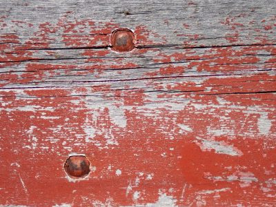 Red paint flakes away, rusty iron bites the wood, grain shows through the age