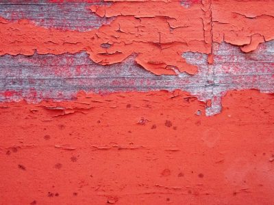Red paint peels away, silvered wood grain shows below, beauty in decay