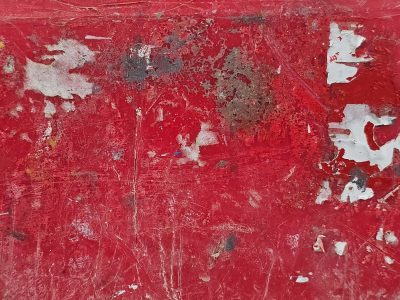 Red paint peels away, white fragments cling to the base, scratches mark the skin