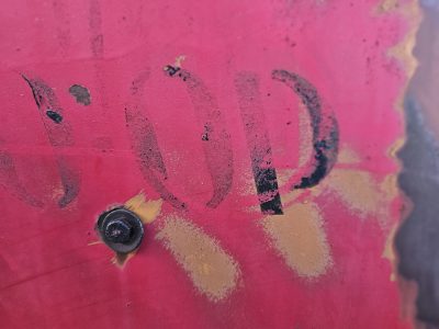 Red paint starts to peel, black letters fade into rust, steel bolt holds its place
