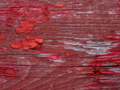 Red strips lift up, grey grain meets the light, weather claims the wood skin