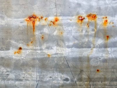 Rust blooms on the grey, orange streaks drip down the steel, metal starts to age