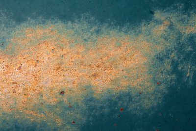 Rust blooms on the teal, orange dust on metal skin, time eats through the paint