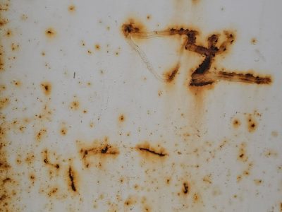 Rust blooms on the white, iron bleeds through the surface, decay claims the steel