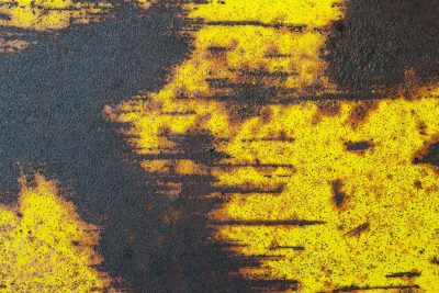 Rust eats yellow paint, dark decay spreads across steel, metal turns to dust