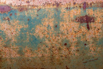 Teal skin flakes away, orange grit claims the surface, years leave a deep trace