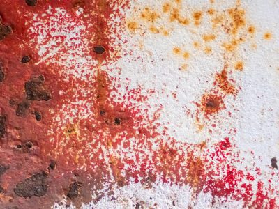 Red paint bleeds away, rust pits mark the metal skin, white gives way to age