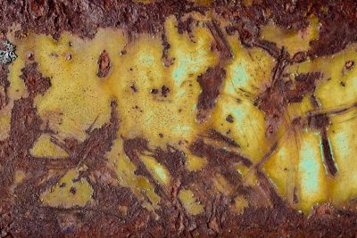 Red rust eats the edge, yellow paint fades into teal, time scars the hard steel