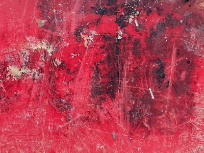 Vibrant red paint scars, black stains bloom in jagged lines, worn surface tells tales