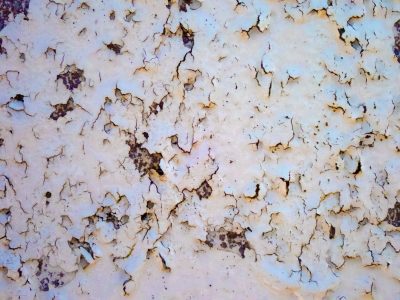 White paint curls away, dark rust pits the metal skin, time breaks down the wall