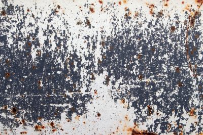 White paint flakes off, dark shadows hide underneath, oxide blooms in spots