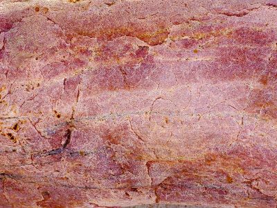 Rose stone etched in light, veins of deep red cross the face, hard earth holds its line