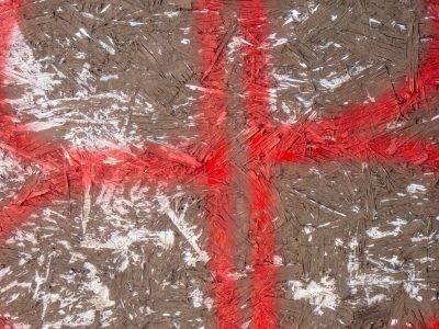 Wood chips pressed and bound, red paint crosses rough surface, fibers catch the light