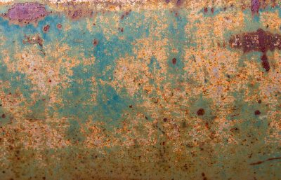 Orange rust blooms wide, teal paint flakes from the surface, metal meets the air