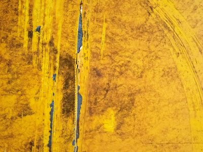 Yellow skin peels back, dark seam splits the weathered plate, rust and dirt remain