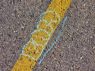 Yellow stripe divides, blue chalk ghost on rough asphalt, sun hits the pavement