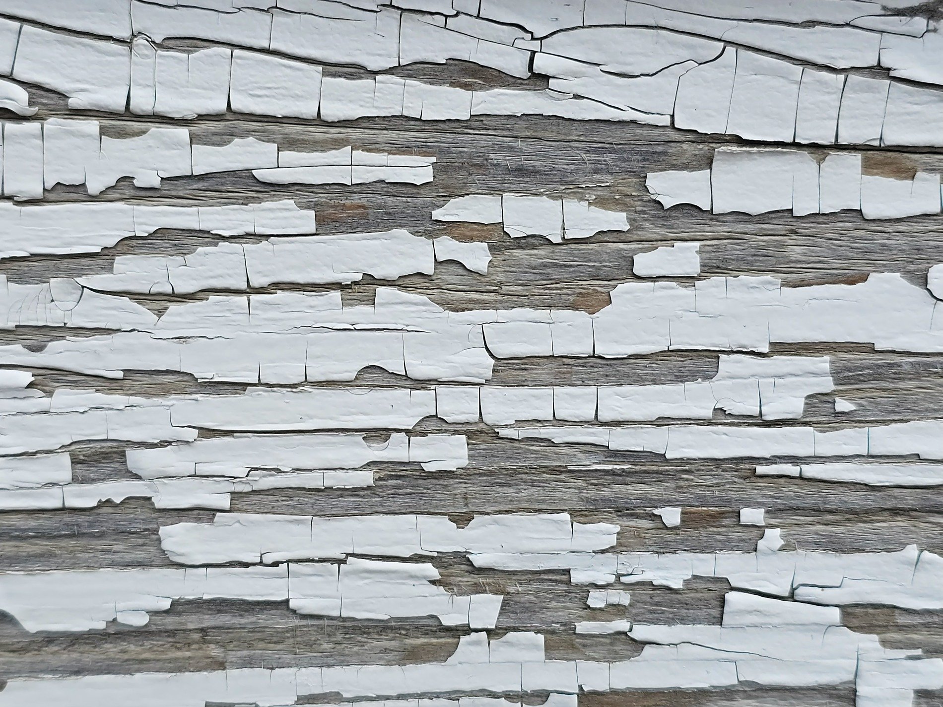 White paint flakes away, weathered grain reveals the age, fragments of the past
