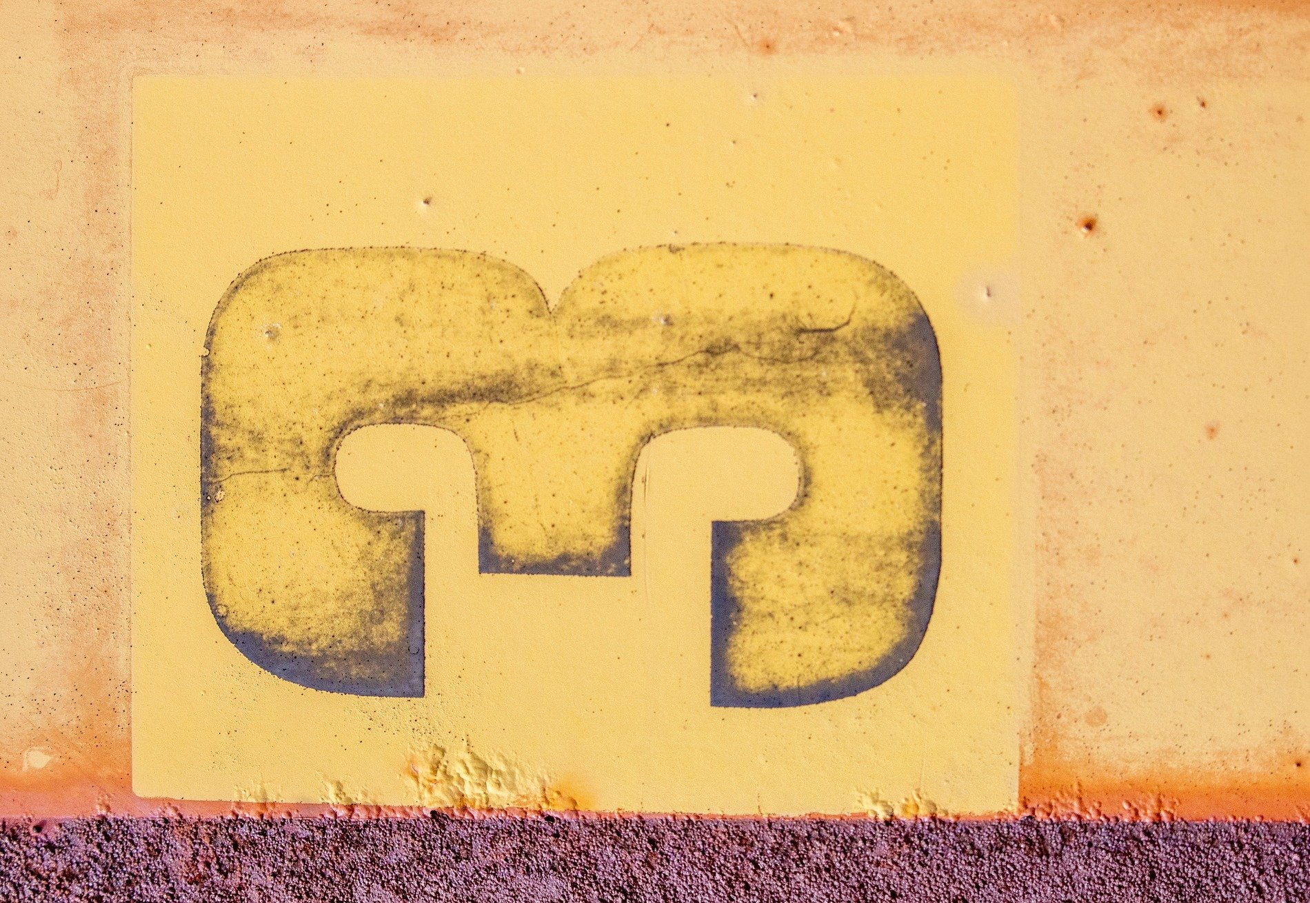 Yellow paint on steel, dark number marks the surface, rust creeps from below