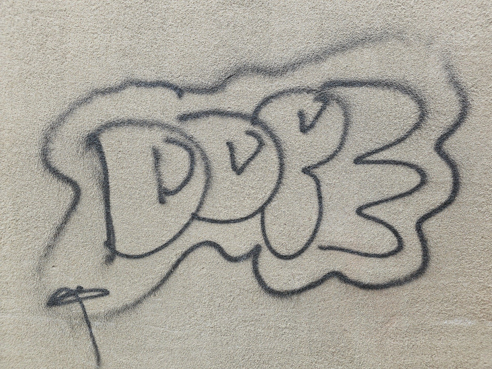 Black ink loops and curls, stone grain beneath spray paint lines, urban marks remain