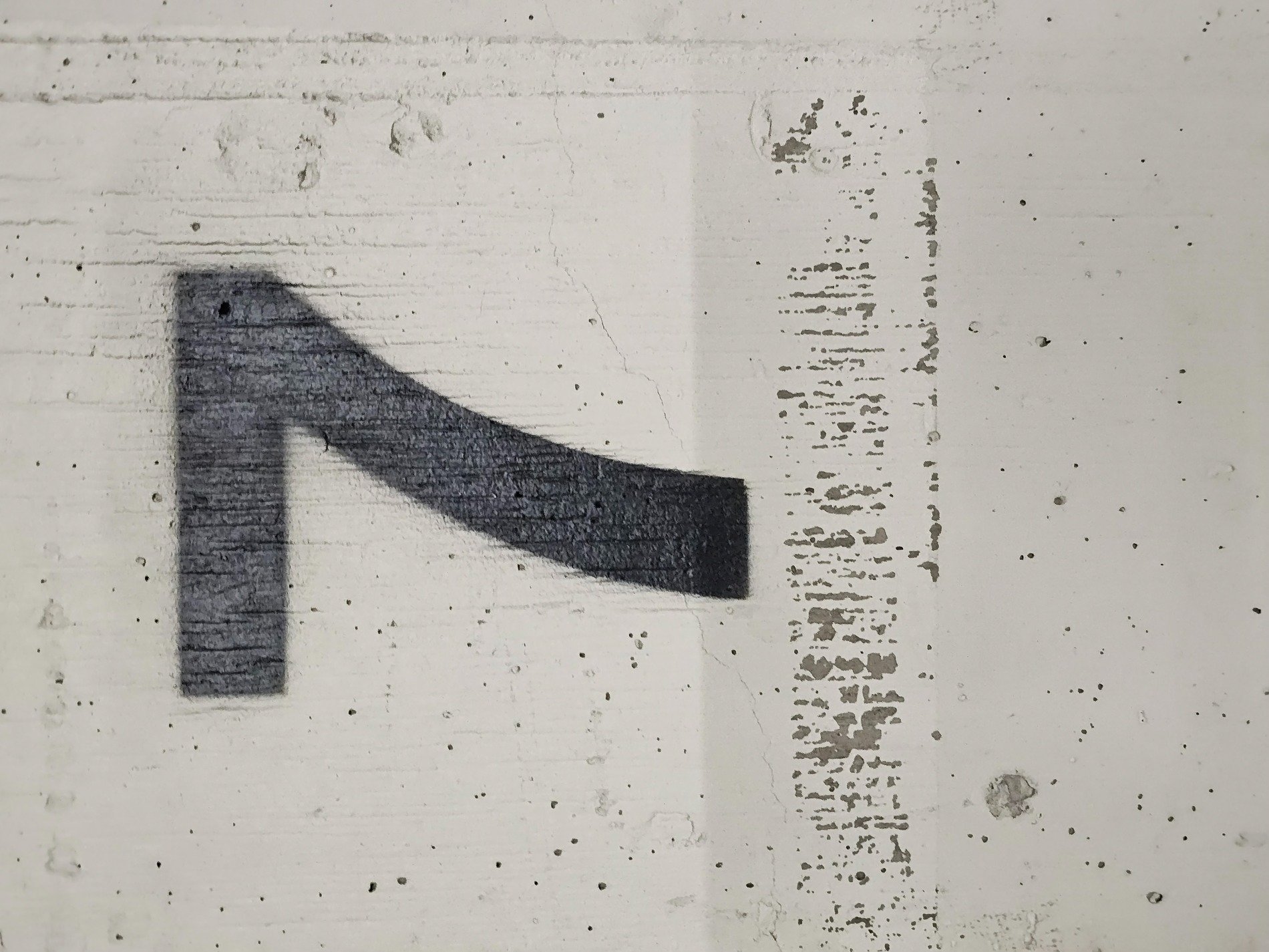 Black ink on concrete, slanted mark defines the space, grit meets painted wall