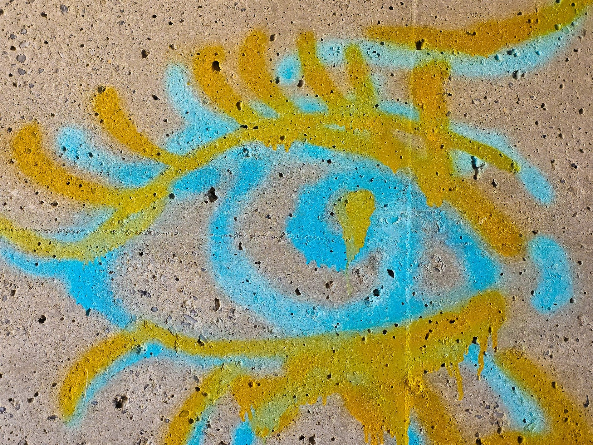 Blue and yellow paint, swirled upon the pitted wall, urban eye looks out