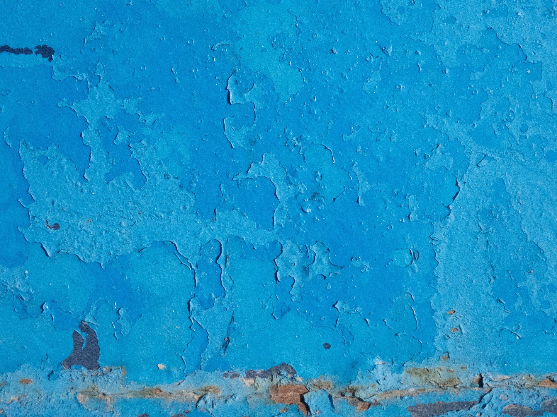 Blue layers chip away, weathered surface curls and falls, rusted edges show