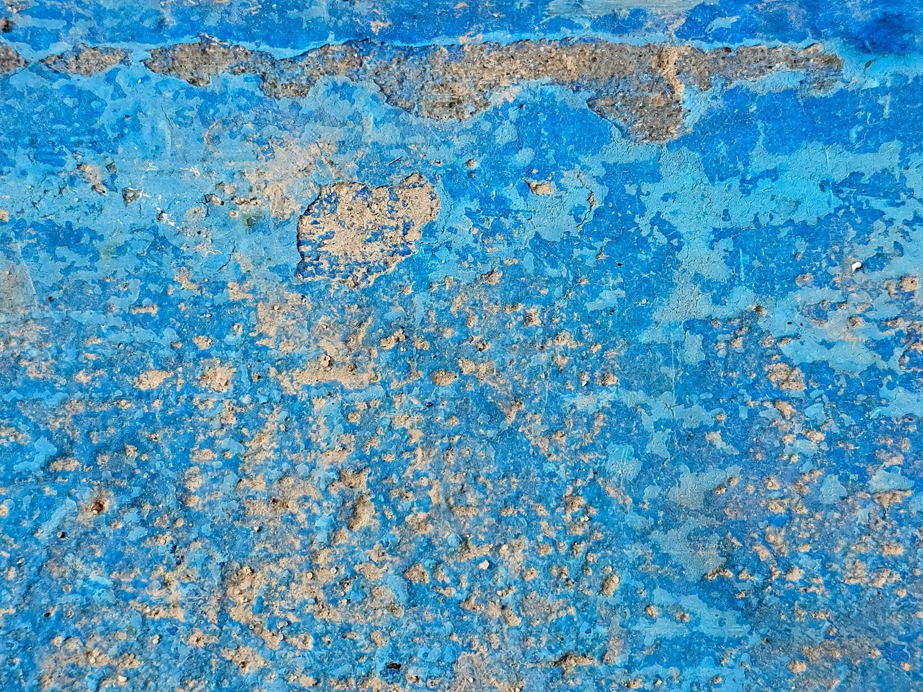 Blue paint chips away, rough concrete hides underneath, time wears down the wall
