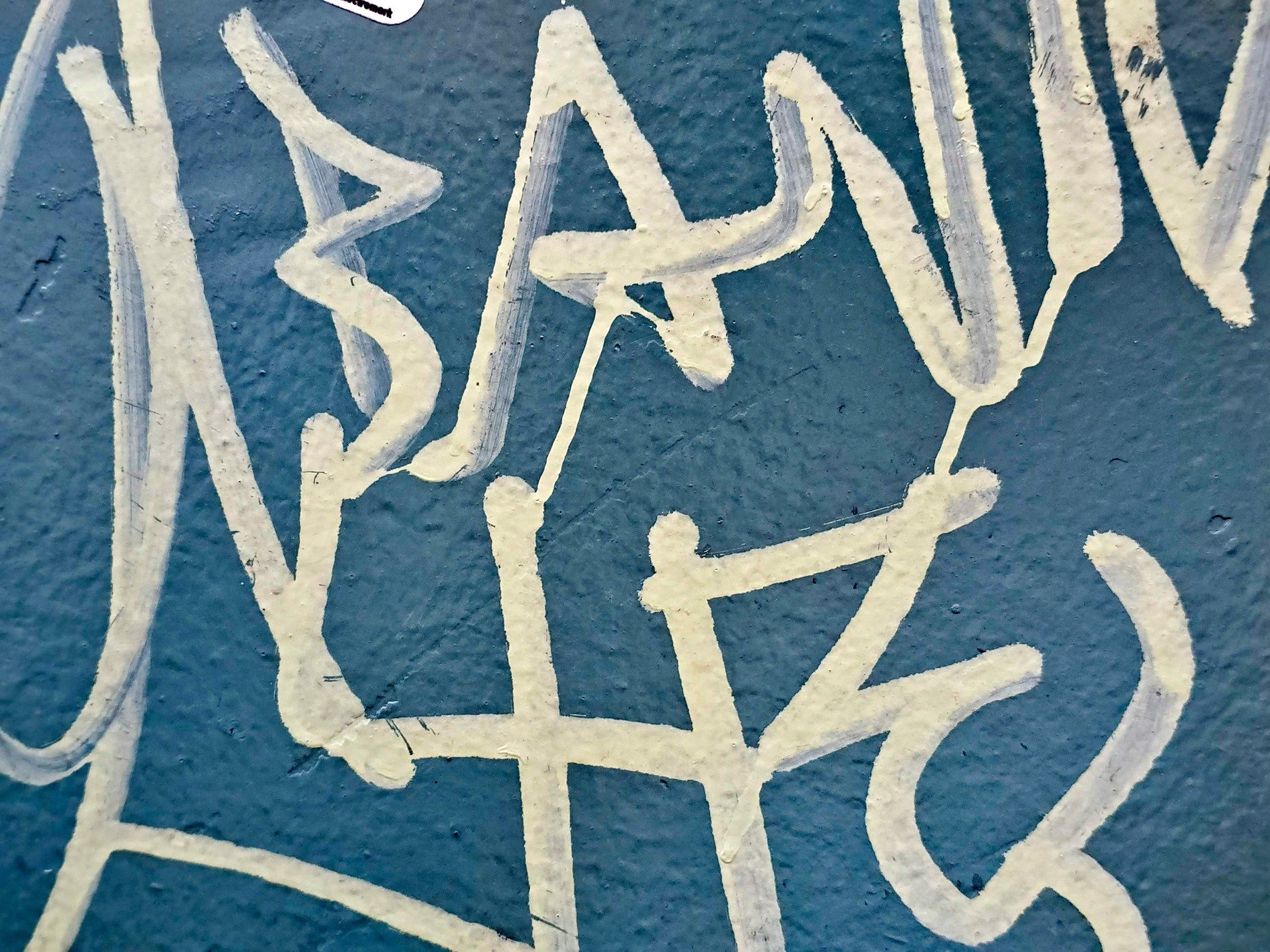 Cream paint on blue, jagged lines form hidden words, texture meets the tag