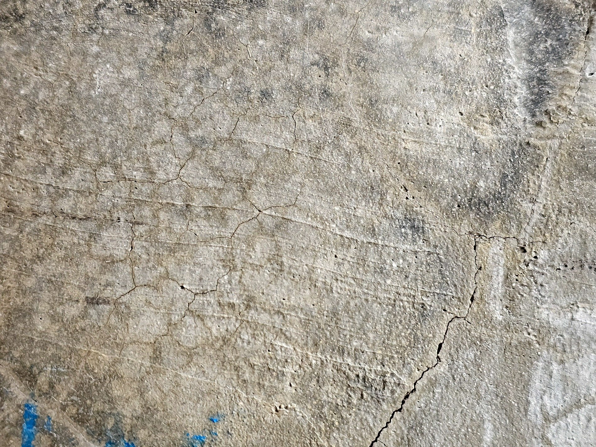 Fissures web the gray, weathered stone bears heavy weight, blue stains mark the edge