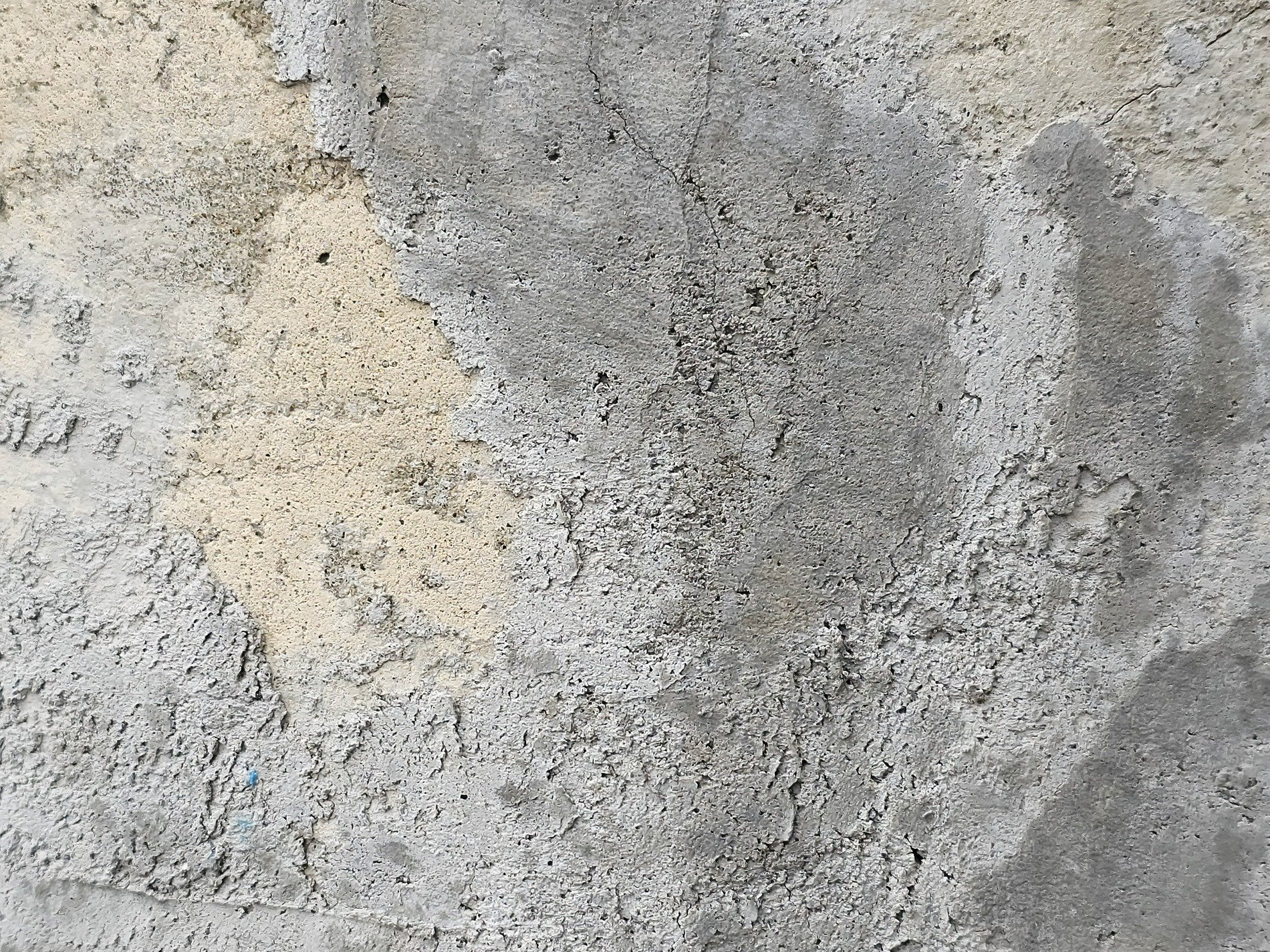 Gray wall wears its age, pitted surface tells a tale, layers fall away