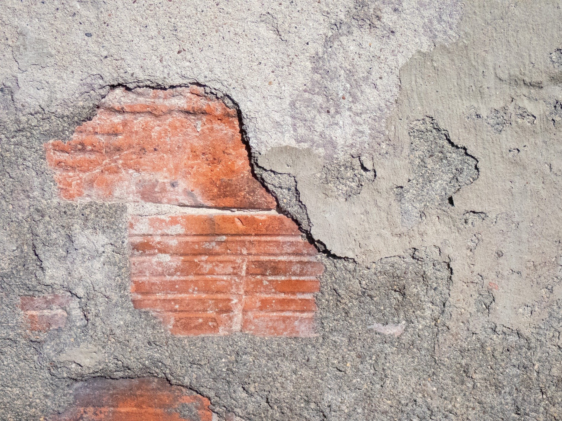 Grey stone falls away, red clay waits beneath the dust, time reveals the wall