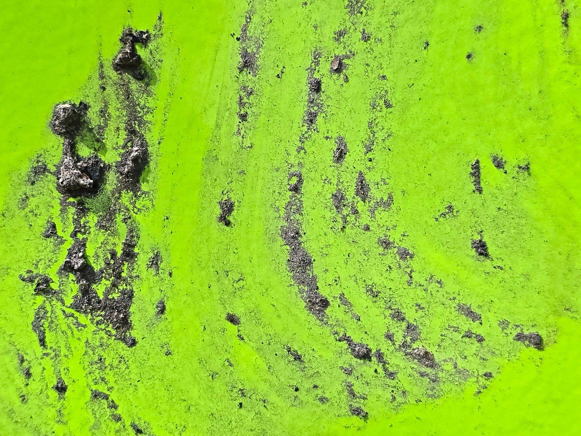 Neon paint recedes, black scars etch the metal skin, rough grit claims the light