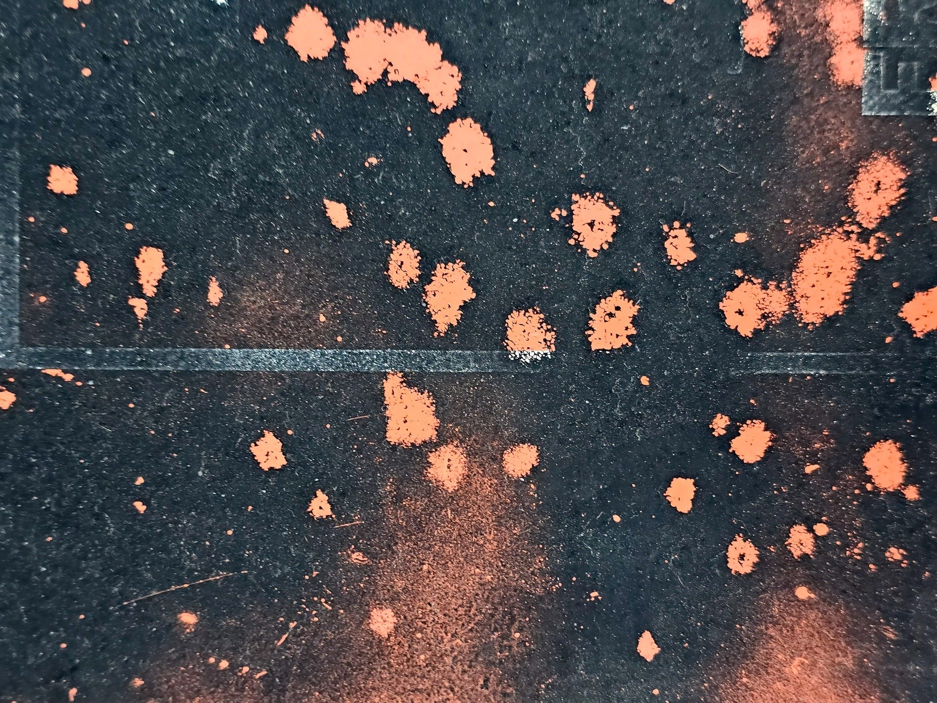 Orange spray on dark, gritty pavement holds the marks, lines fade into black