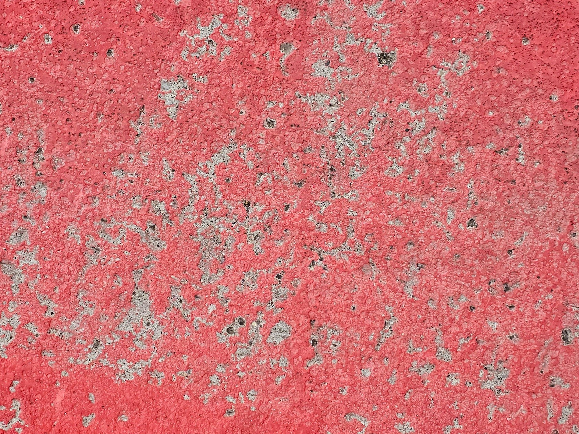 Red paint wears away, grey concrete breaks the surface, time erodes the hue