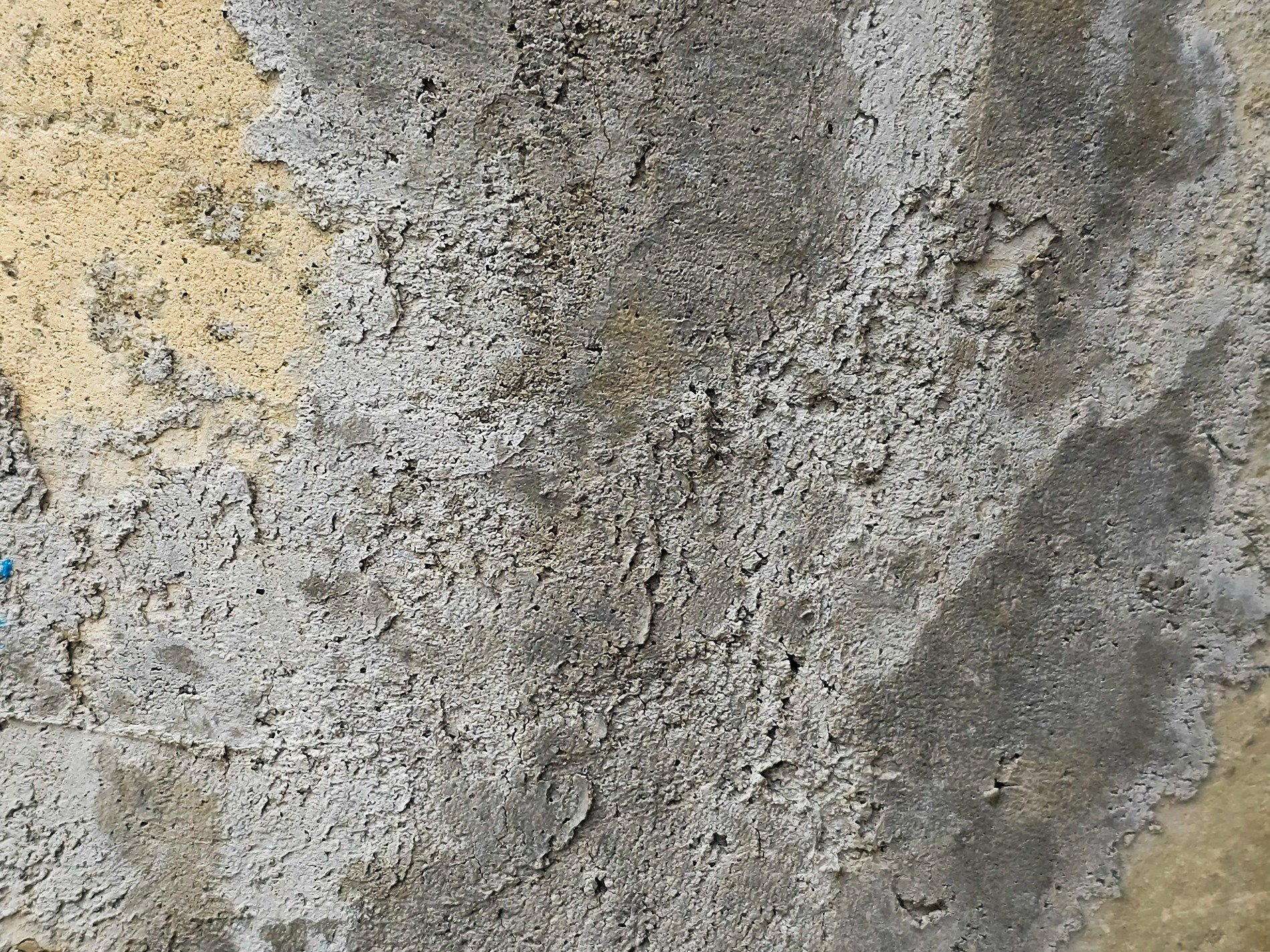 Rough gray wall stands worn, layers peel from gritty stone, time wears down the face