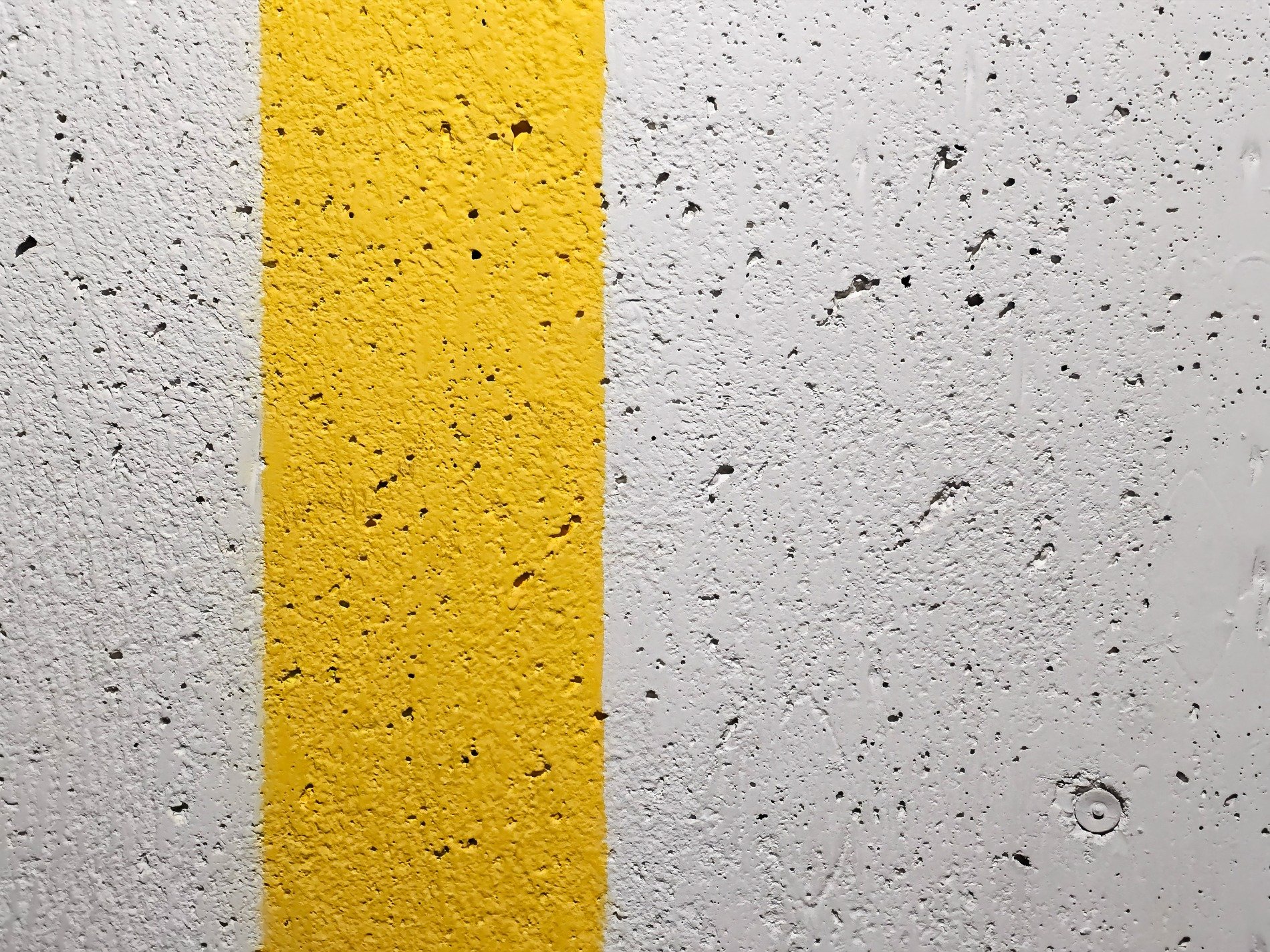 Rough wall of concrete, yellow stripe divides the grey, pitted paths remain