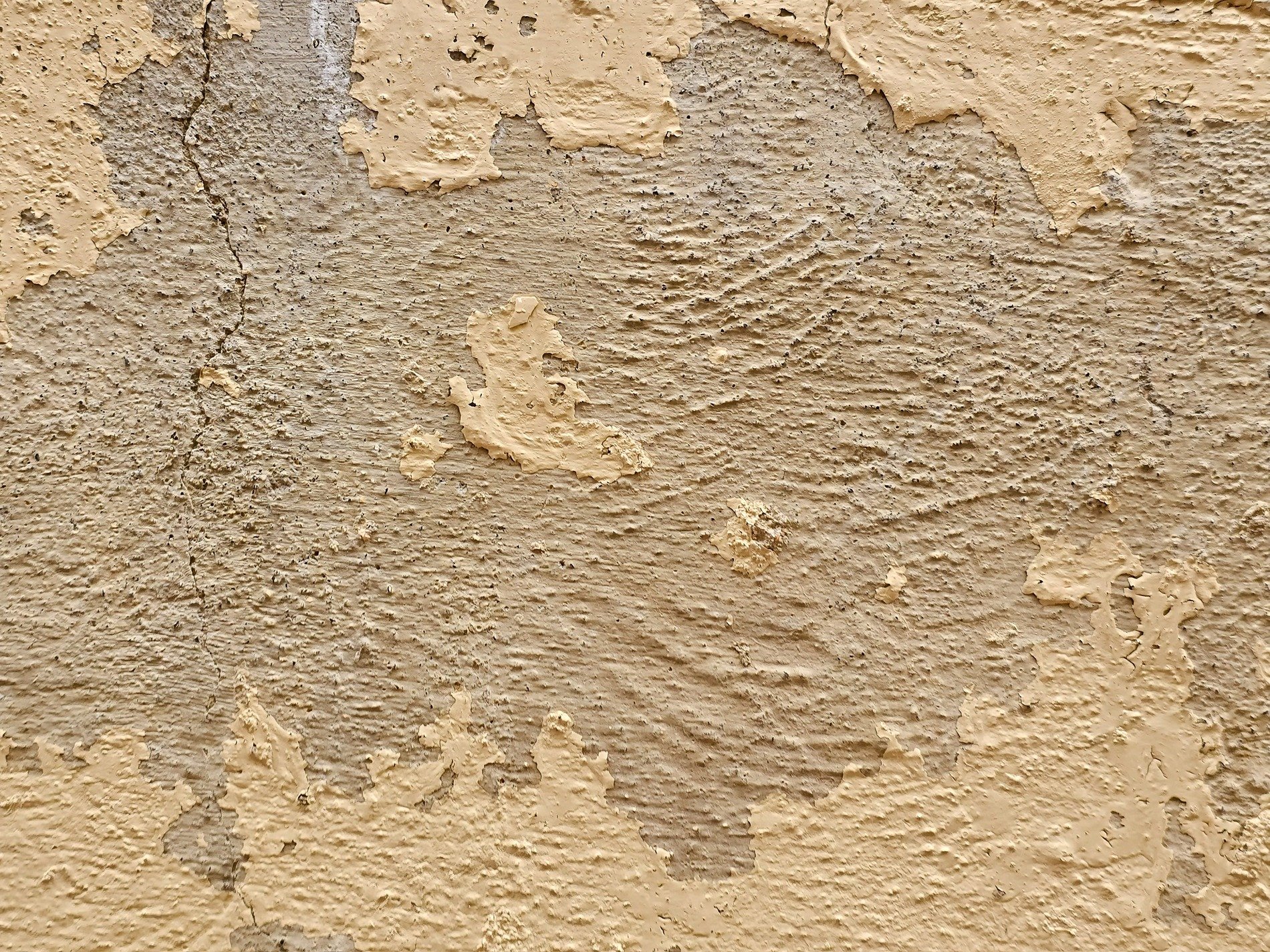 Tan paint flakes away, rough stone ridges hide beneath, time cracks the surface